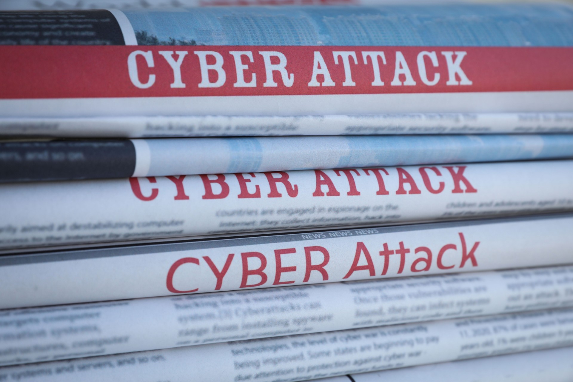 Stacked newspapers with headlines CYBER ATTACK as background, closeup